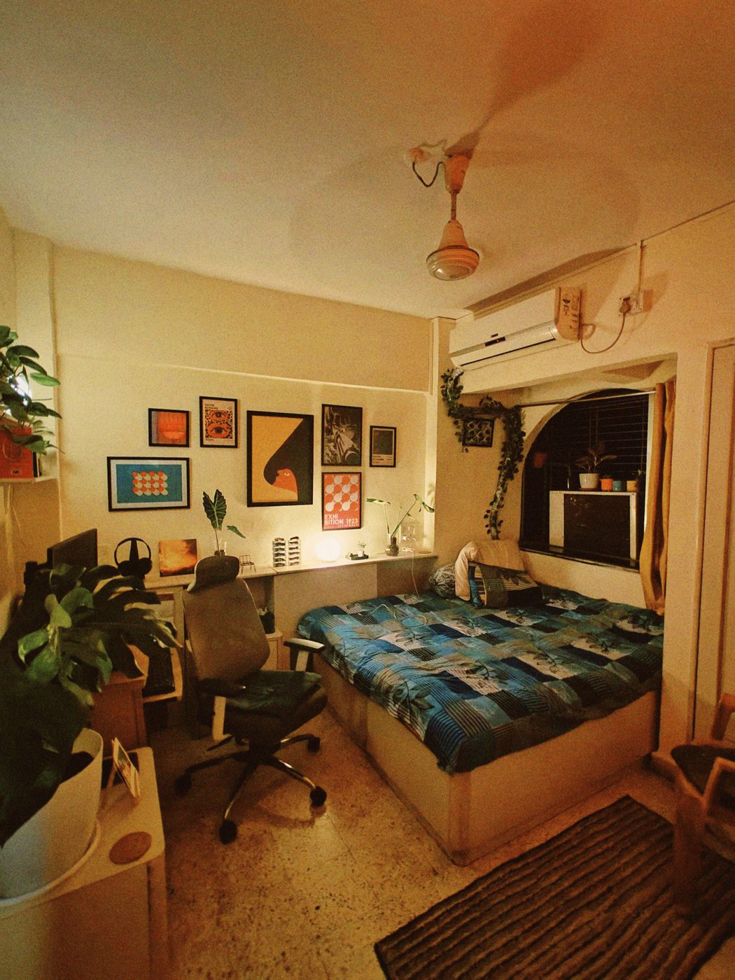 A desk under a wall of framed prints, with plants and a monitor